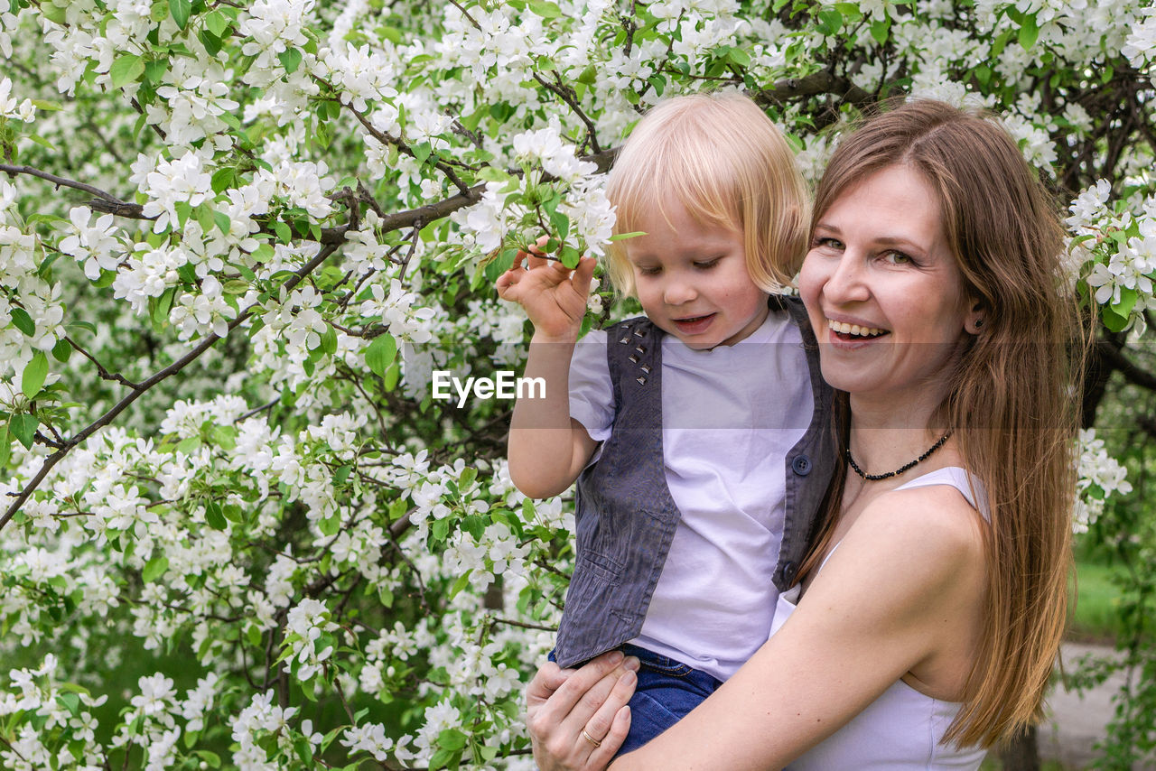 Mother and son enjoying a serene moment in a spring garden surrounded by fragrant apple blossoms.