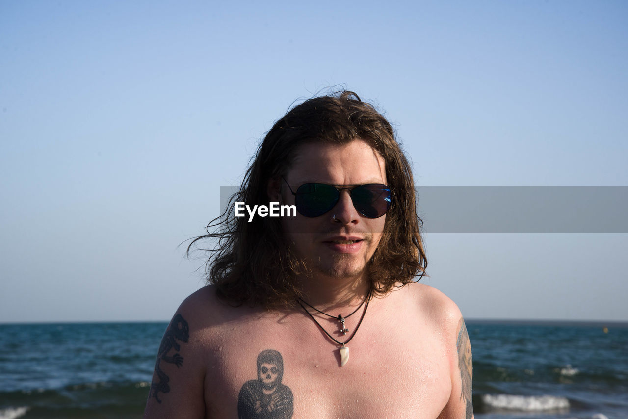 Shirtless man at beach against clear sky