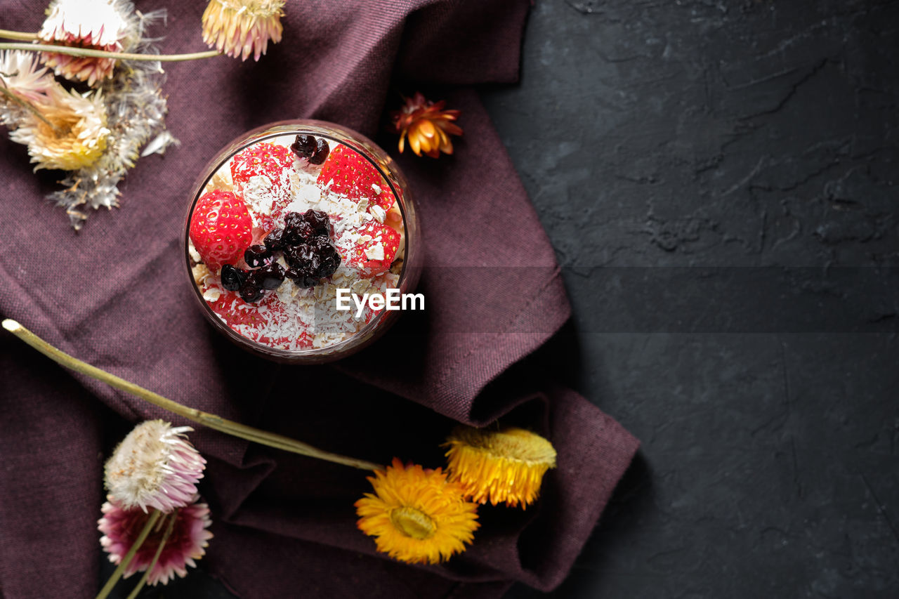 Top view appetizing smoothie bowl with granola strawberries and blueberries placed on table near various wildflowers