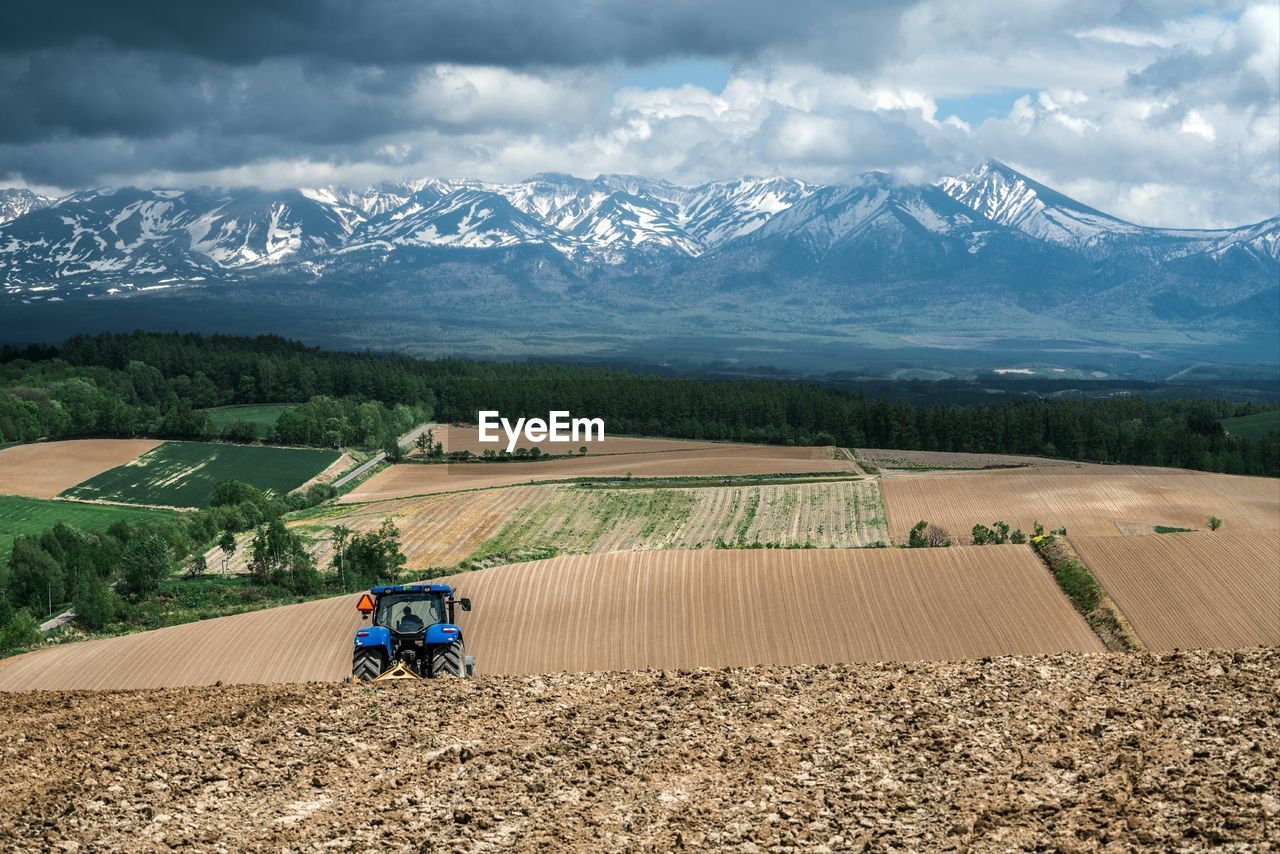 Tractor ploughing farmland on rolling hills against a mountain backdrop