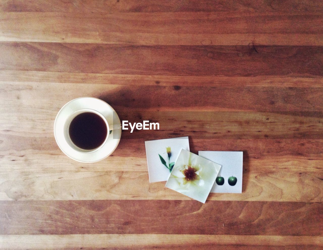 Directly above shot of black coffee and pictures on wooden table