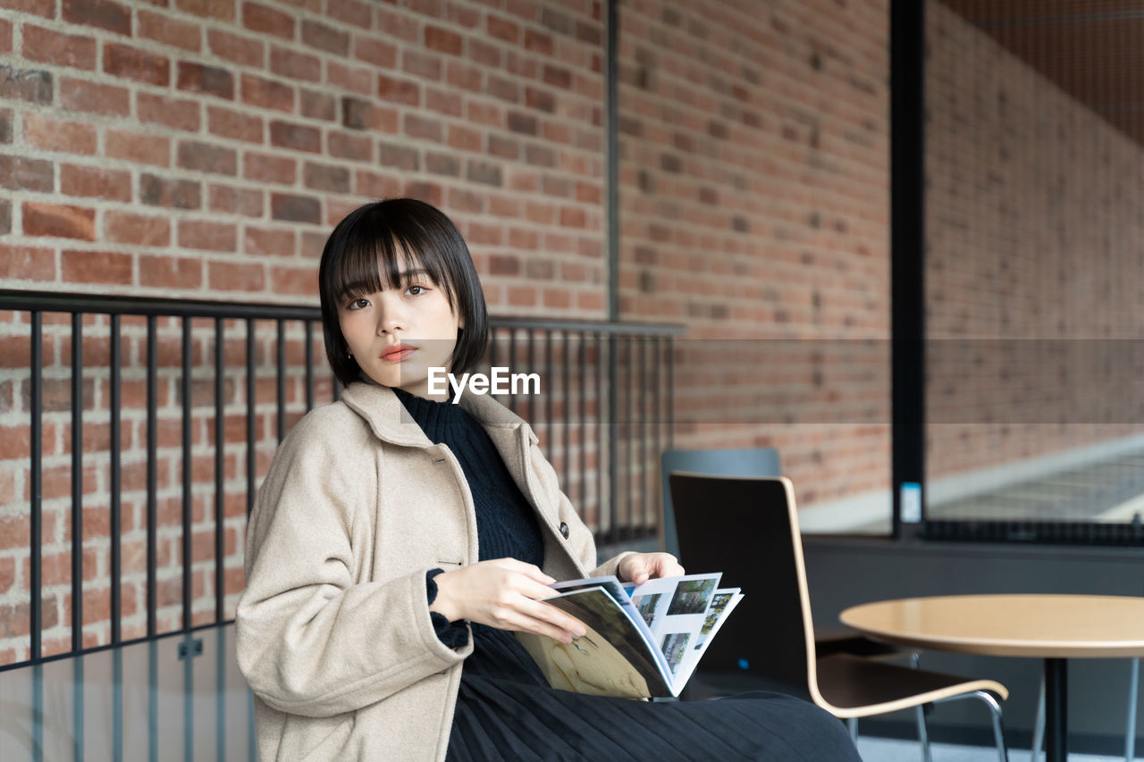 Young woman using mobile phone while standing against wall