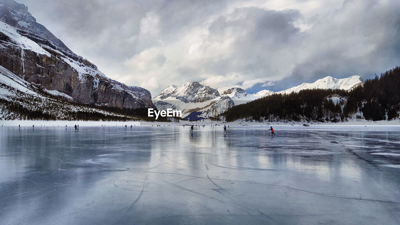 People skiing on frozen lake against sky