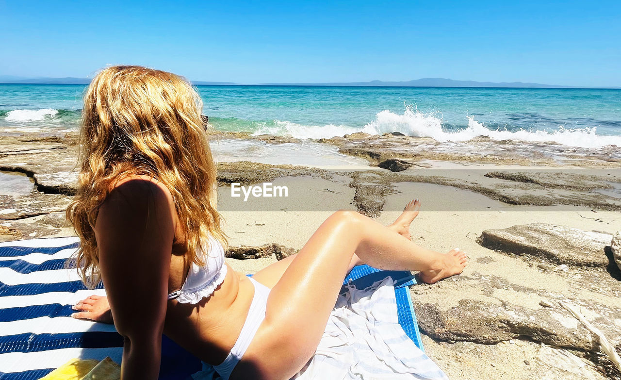 Rear view of woman sitting at beach against sky