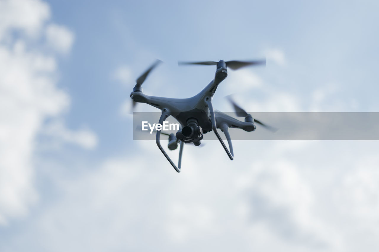 Low angle view of drone flying against cloudy sky