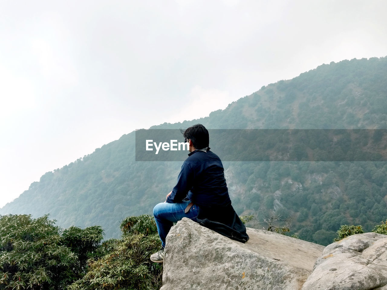 Rear view of man sitting on mountain against sky