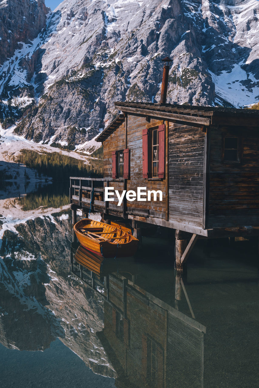 Boat moored by wooden cabin against snowcapped mountain