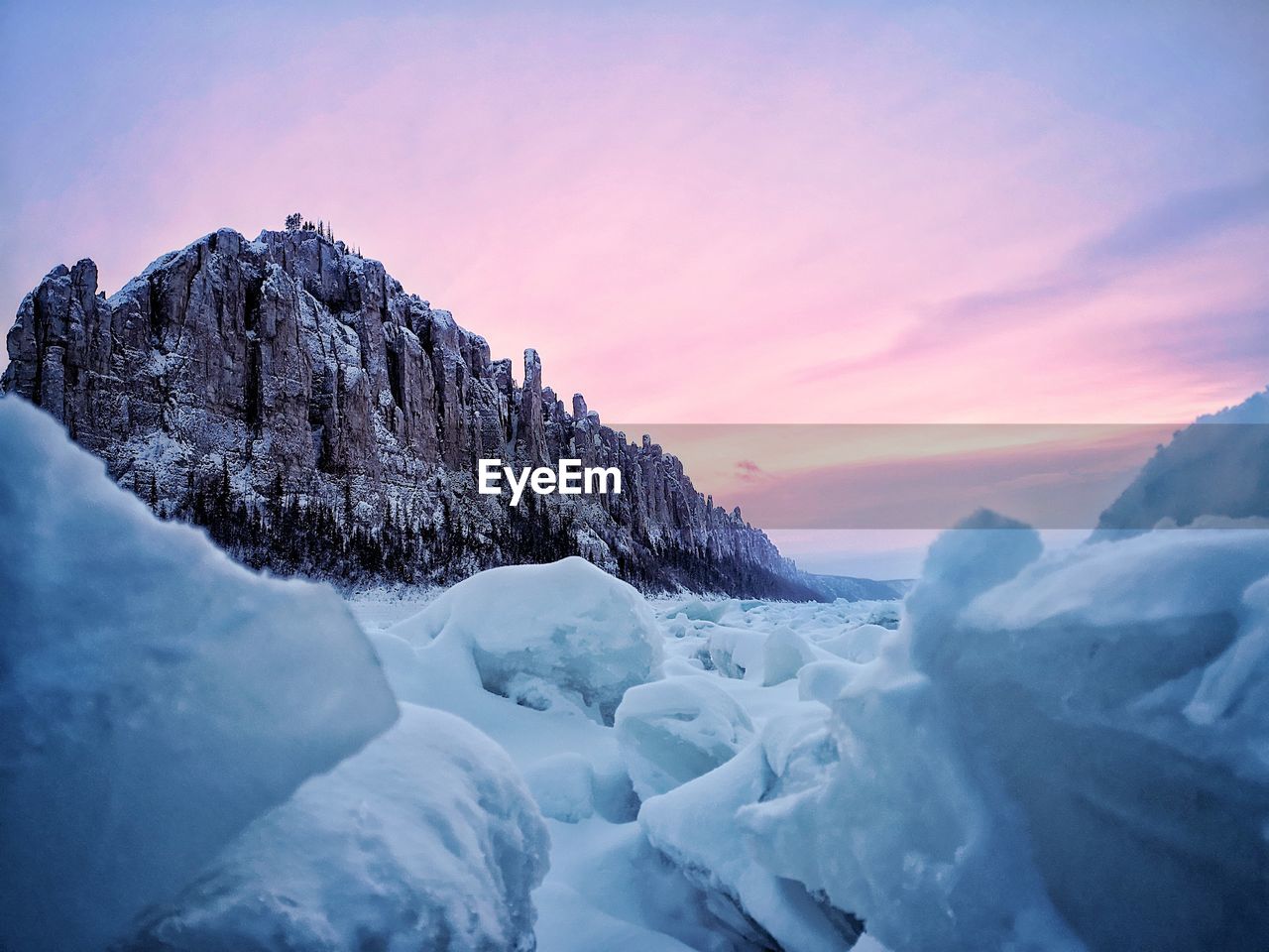 Scenic view of glacier against rock mountain during sunset