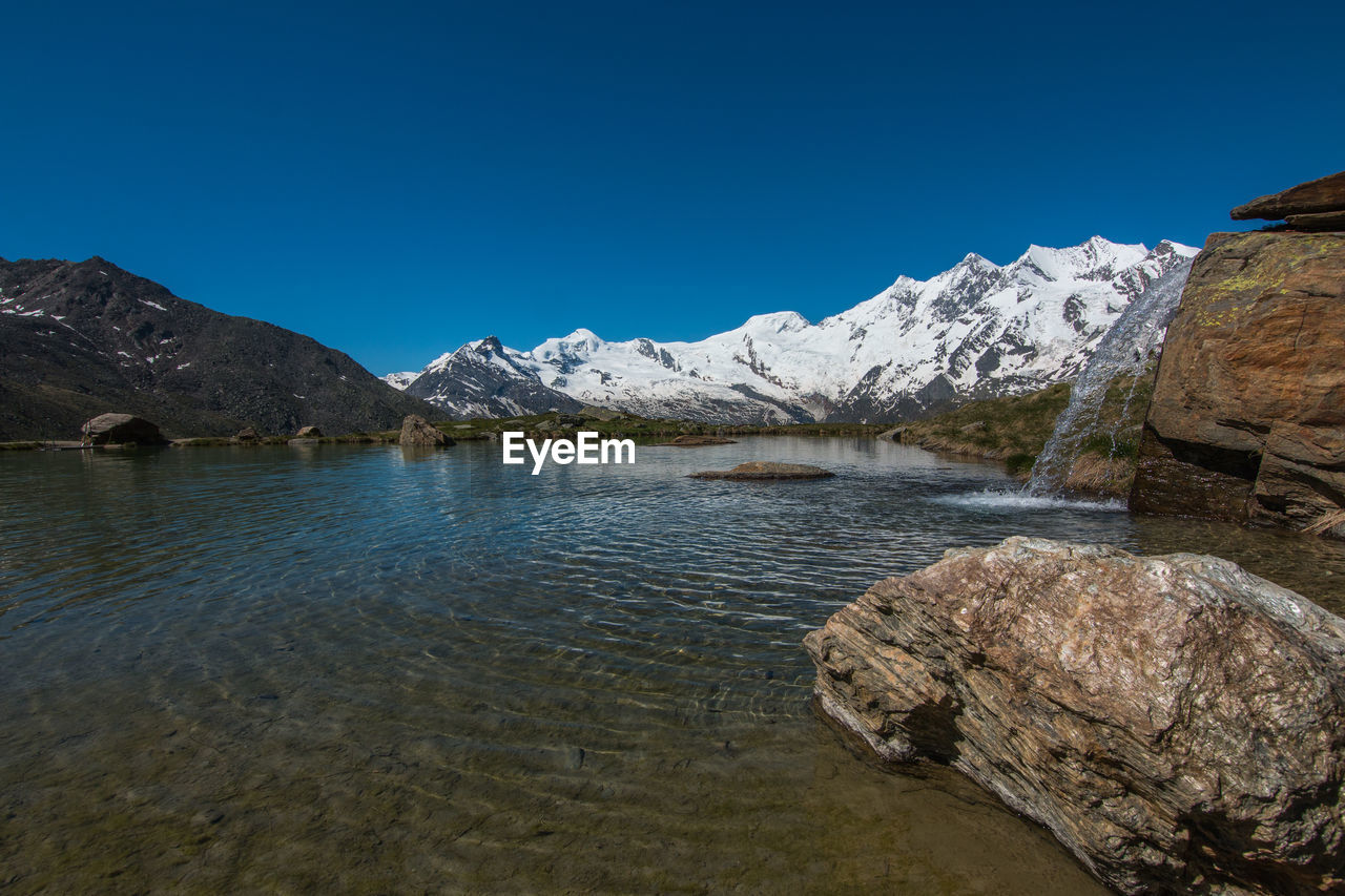 Scenic view of lake and mountains against clear blue sky
