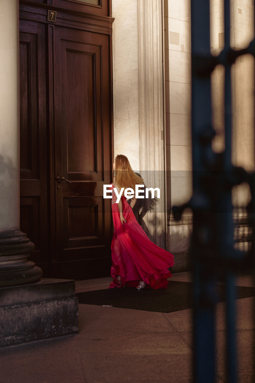 Full length of woman wearing red evening gown walking towards door