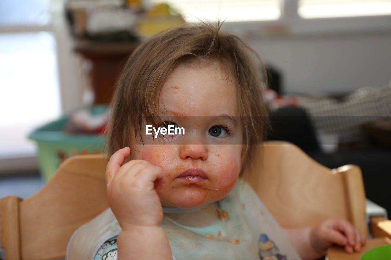 Close-up of cute baby girl with messy face looking away while sitting on chair at home