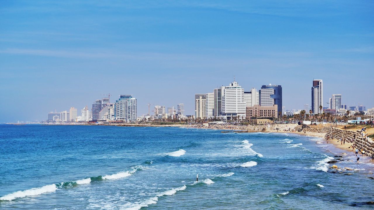 Sea by city buildings against blue sky