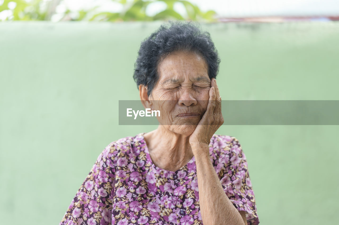 Senior black-haired woman touching the mouth with hand with painful expression because of toothache 