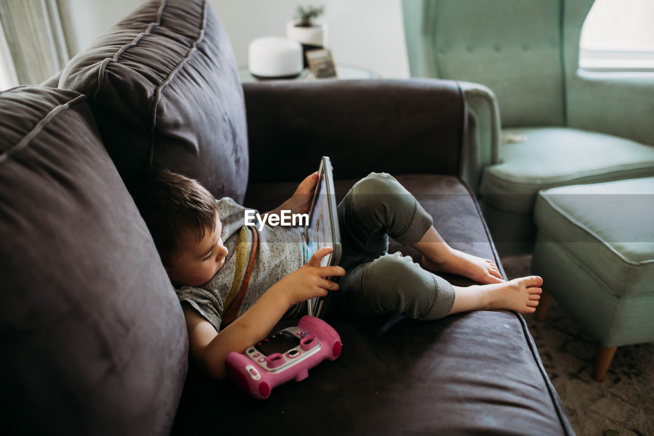 Young boy sitting on couch playing educational game on tablet
