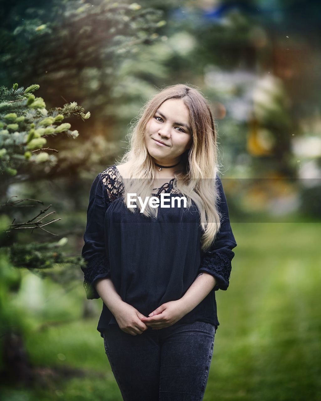 YOUNG WOMAN STANDING AGAINST PLANTS