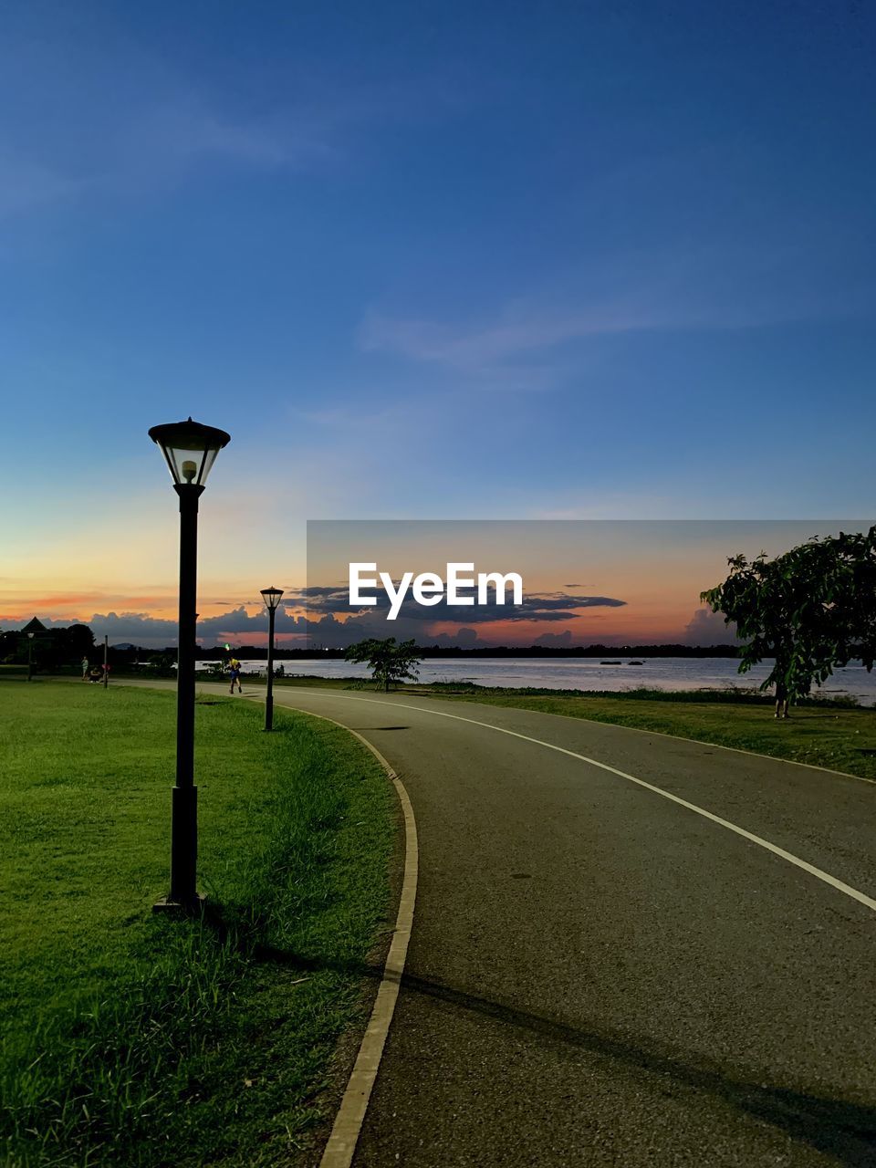 sky, horizon, sunset, dusk, nature, road, evening, street, grass, street light, cloud, plant, no people, transportation, environment, light, tree, landscape, sunlight, beauty in nature, scenics - nature, lighting equipment, outdoors, tranquility, land, blue, city, tranquil scene, architecture, reflection, travel destinations, travel