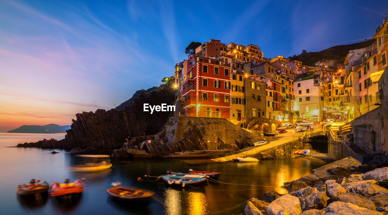 ILLUMINATED BUILDINGS BY SEA AGAINST SKY AT NIGHT