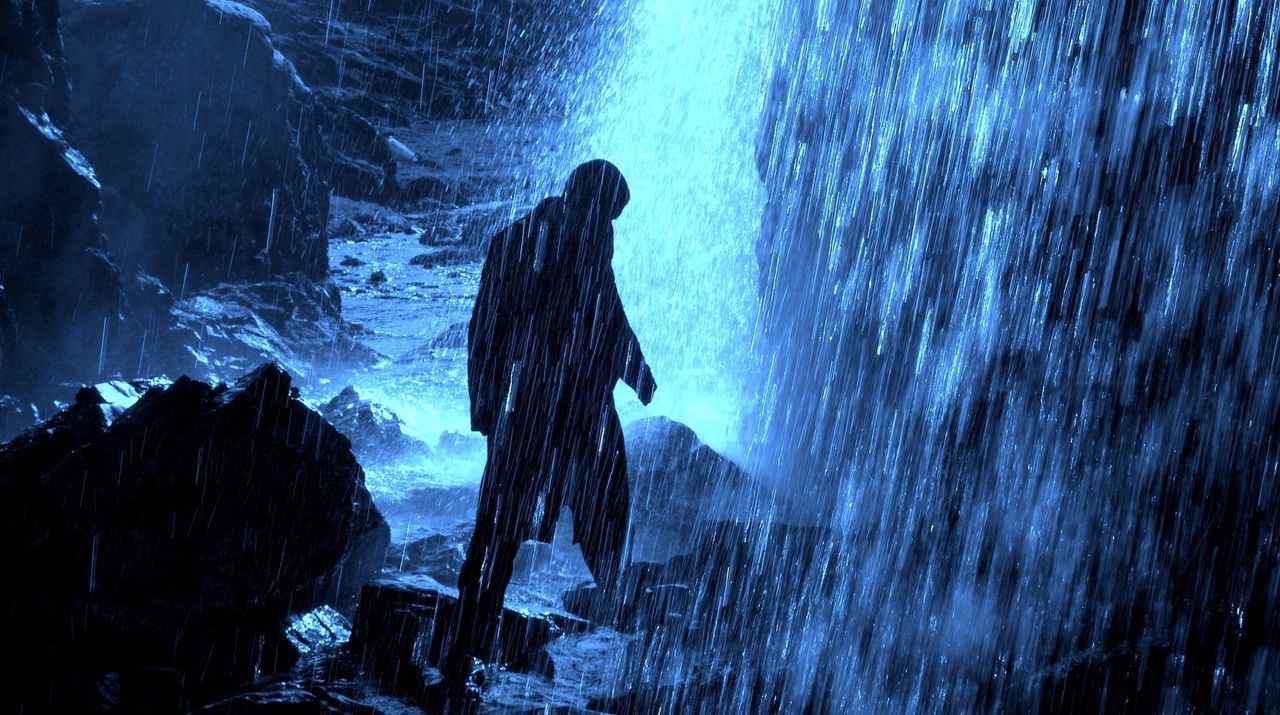 Silhouette man standing on rocks under waterfall