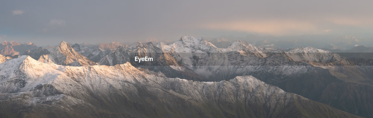 Panoramic shot of snowy mountain range with high peaks during orange sunset, austrian alps, europe