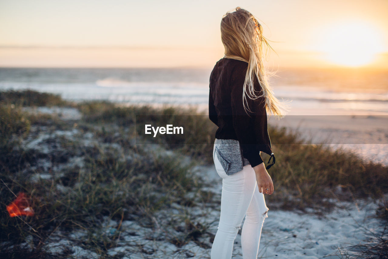 Young woman walking at beach against clear sky during sunset