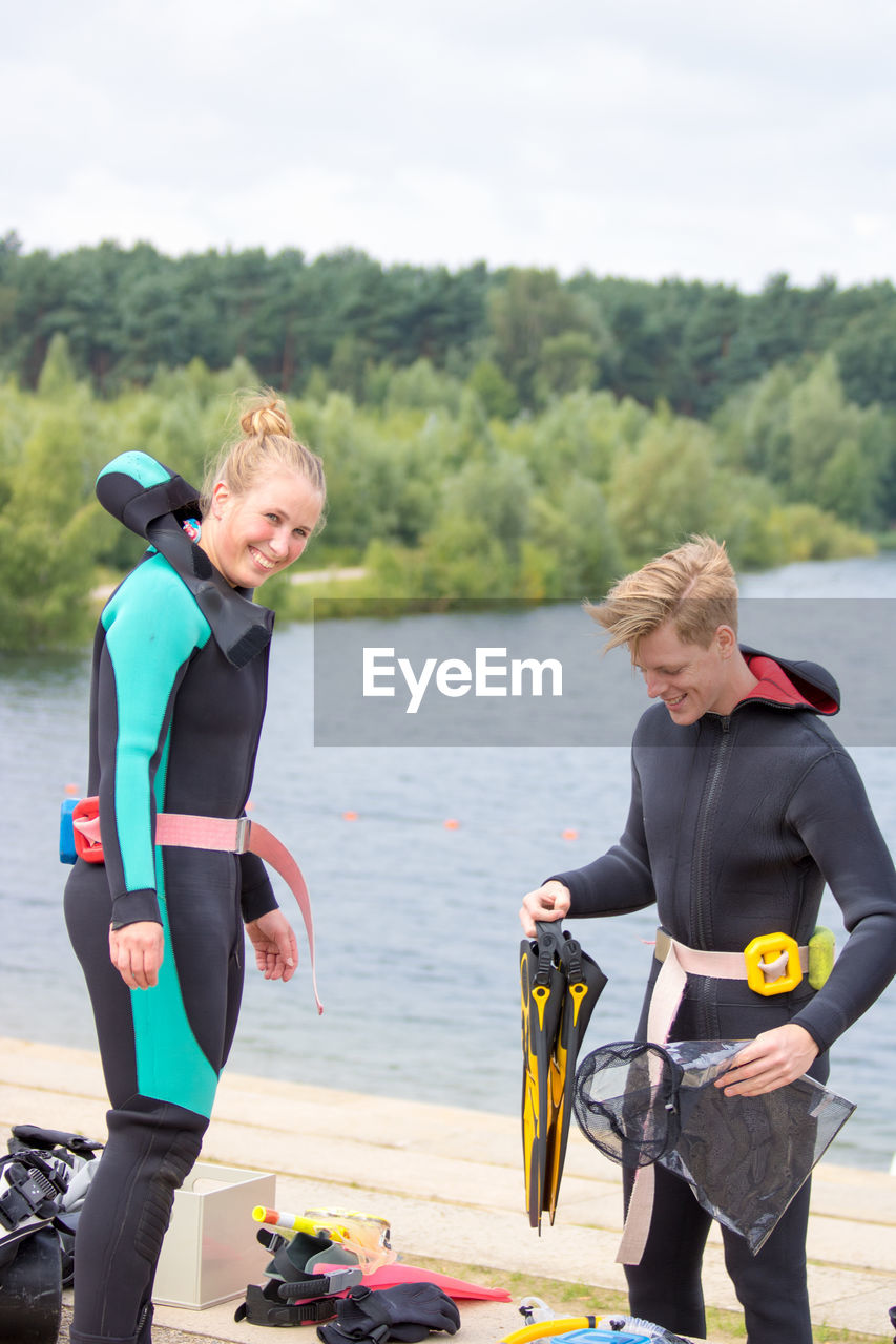 Portrait of happy woman with friend preparing for scuba diving by lake