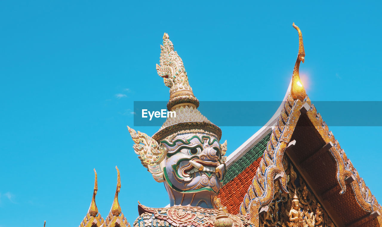 Low angle view of temple against building against clear blue sky and a demon statue in bangkok