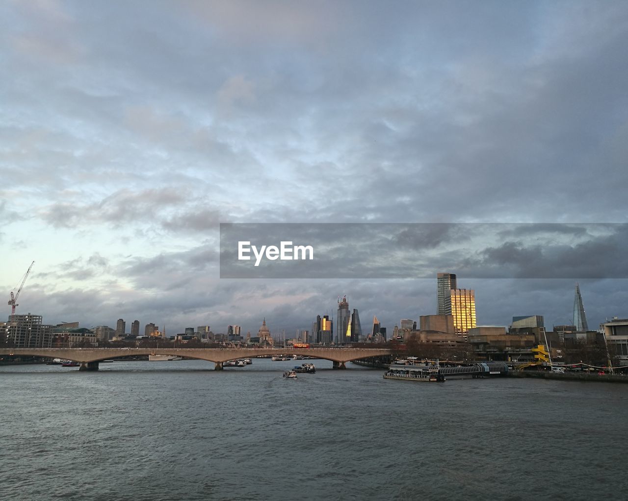 View of buildings by river against cloudy sky