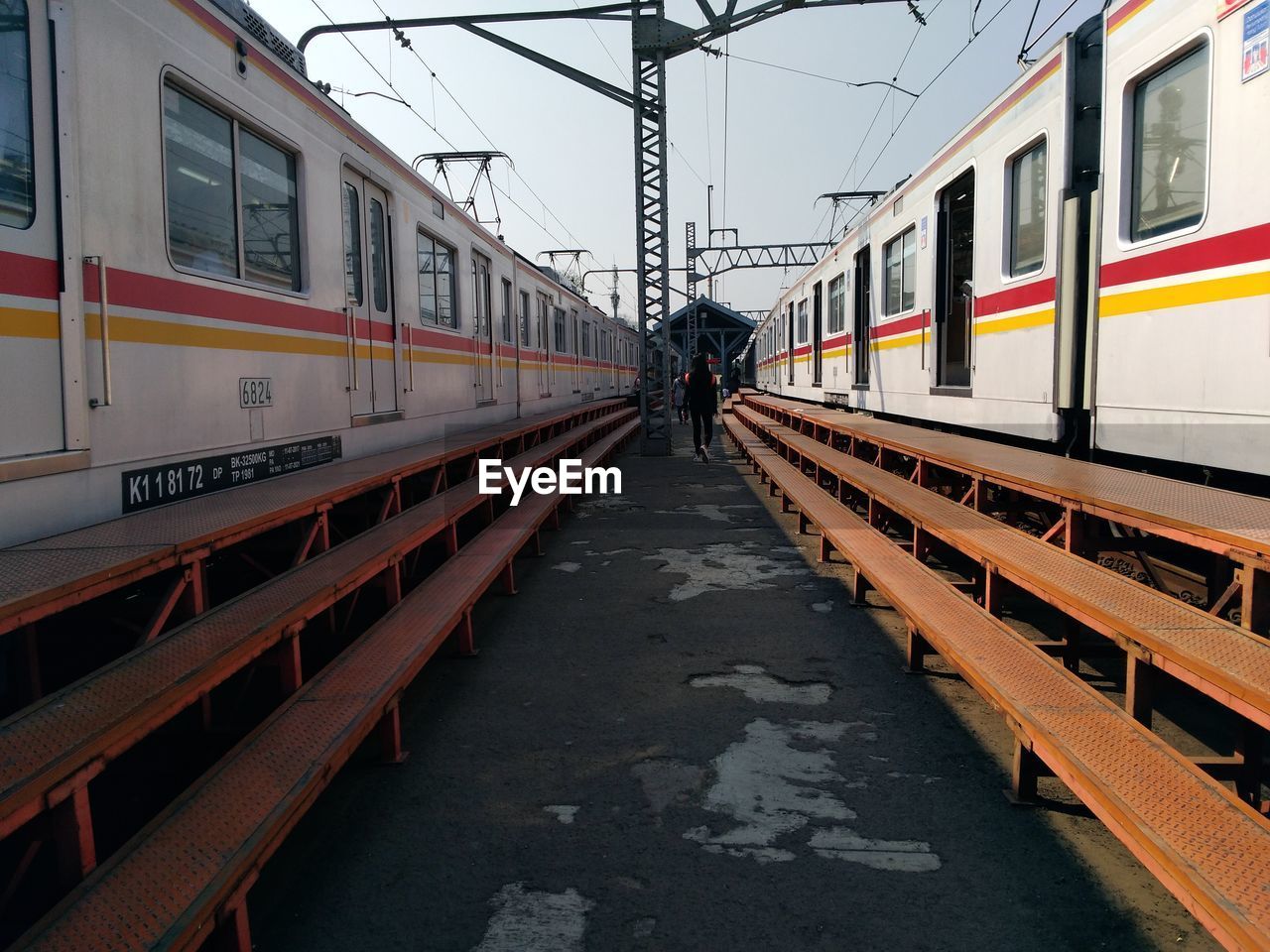 Rear view of woman walking amidst trains at railroad station platform