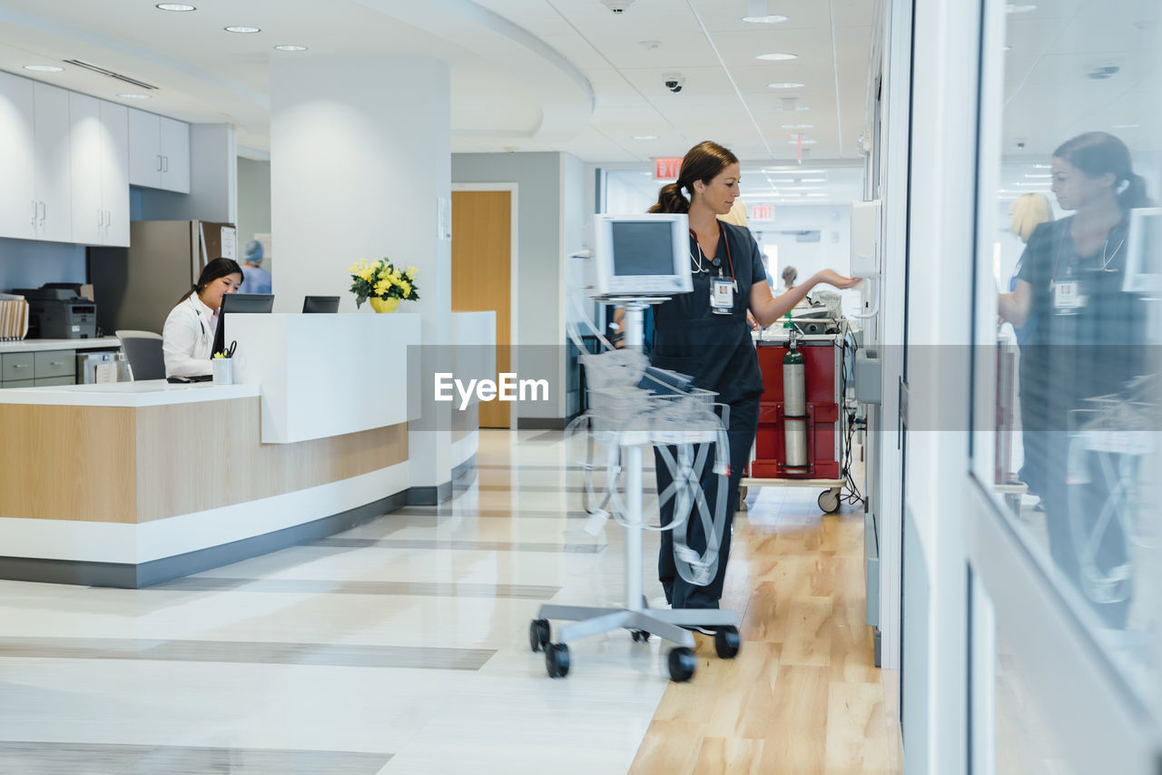 Female doctor working at reception while nurse using sanitizer by monitoring equipment at hospital