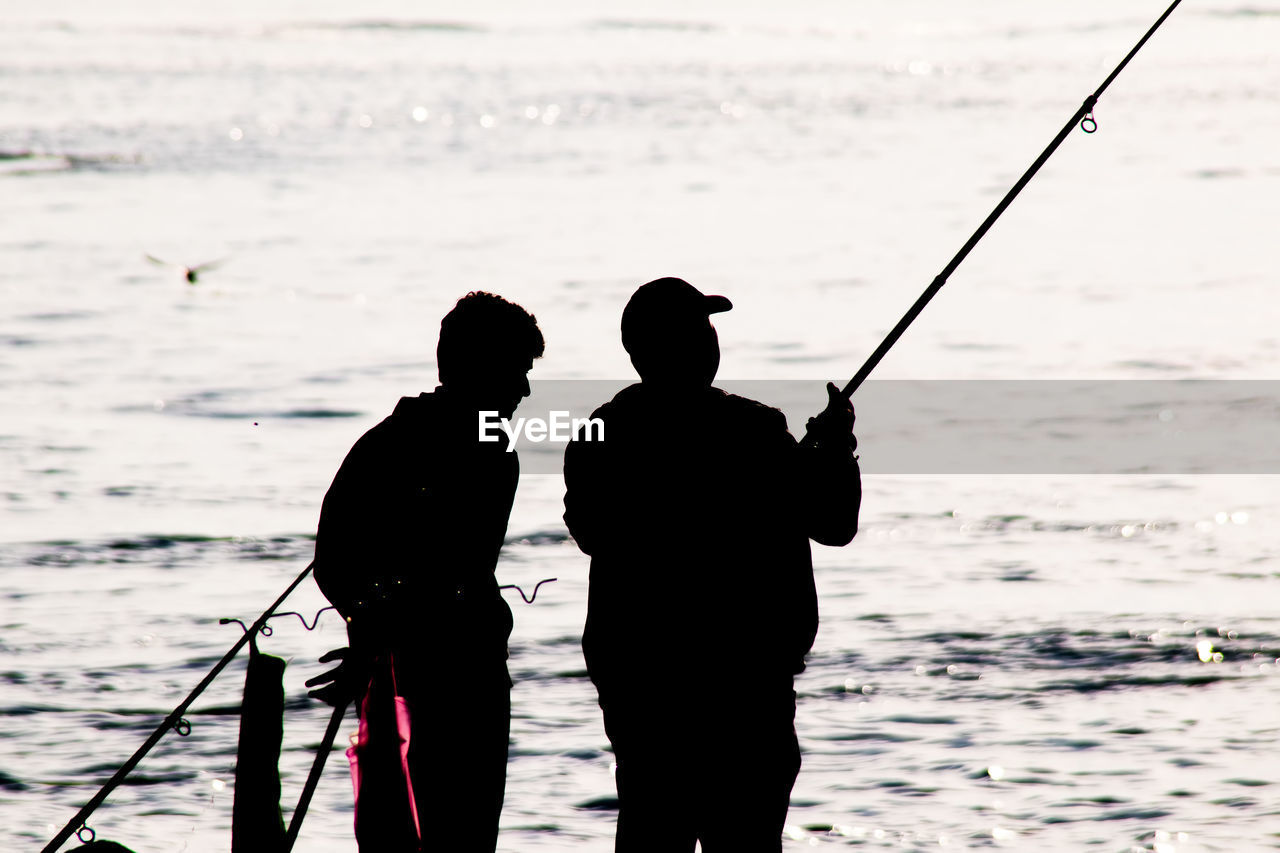 REAR VIEW OF SILHOUETTE MAN FISHING ON SEA SHORE