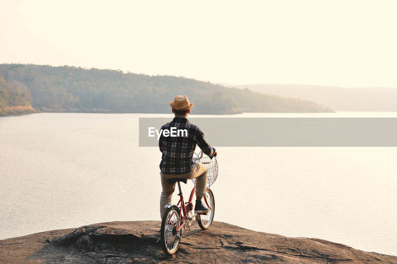 Rear view of man with bicycle on water against sky