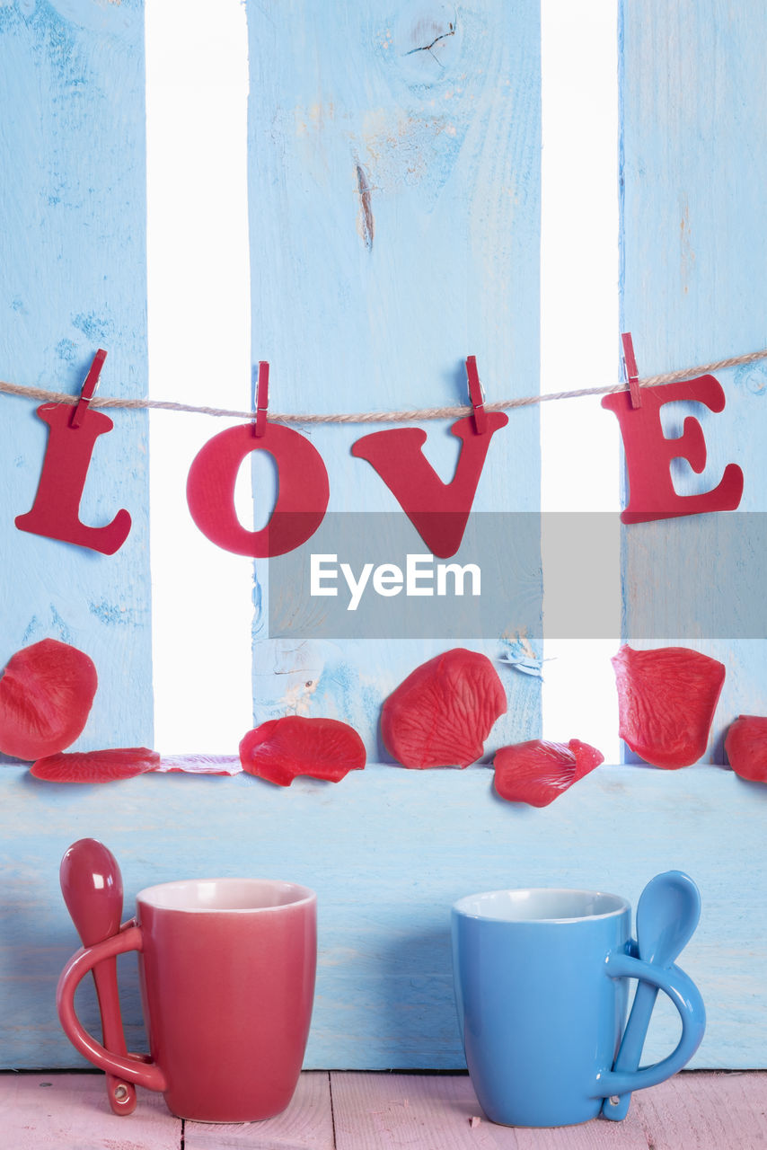 Close-up of love text hanging over petals and mugs