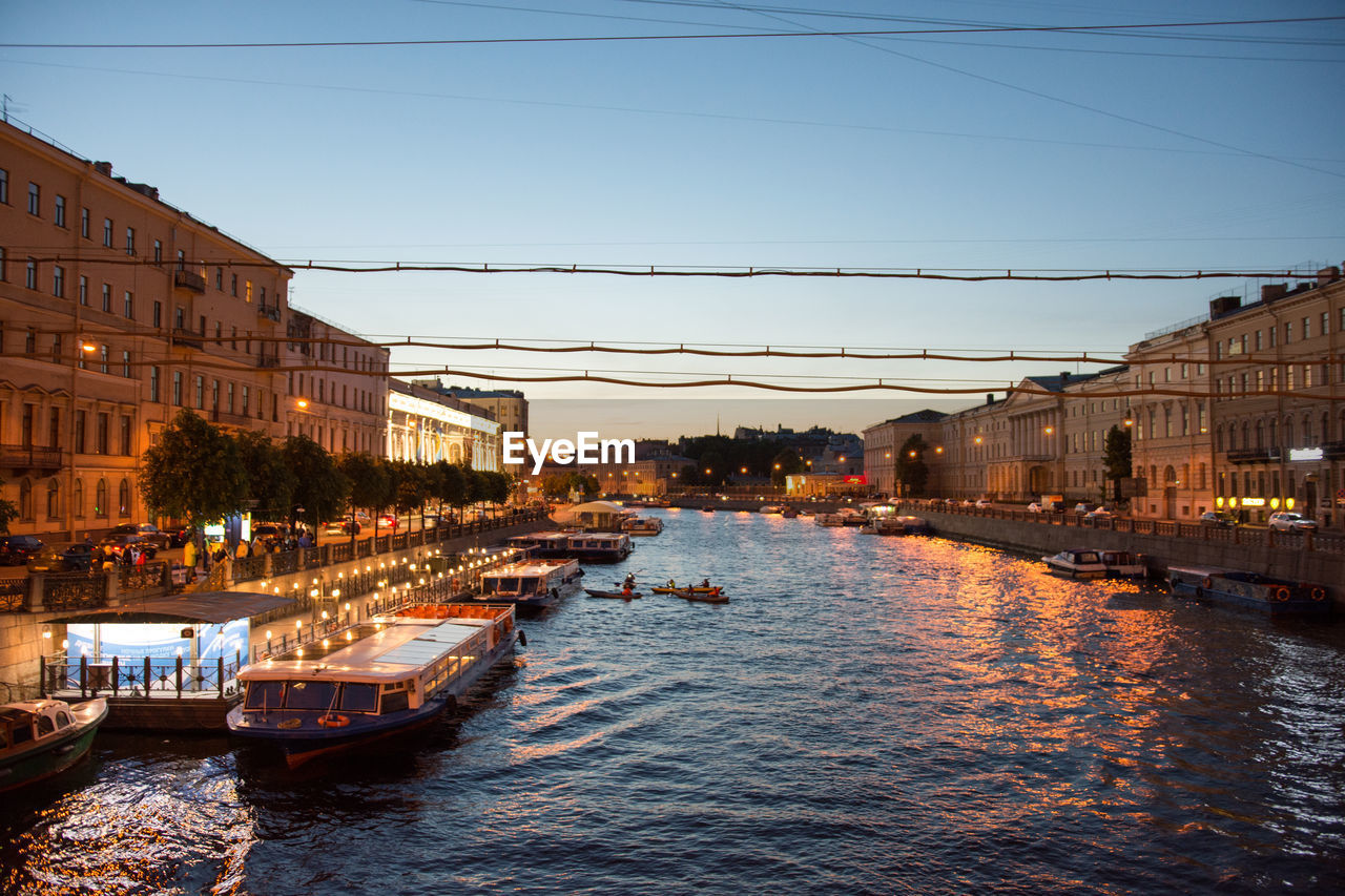 Canal amidst illuminated buildings in city against clear sky at dusk