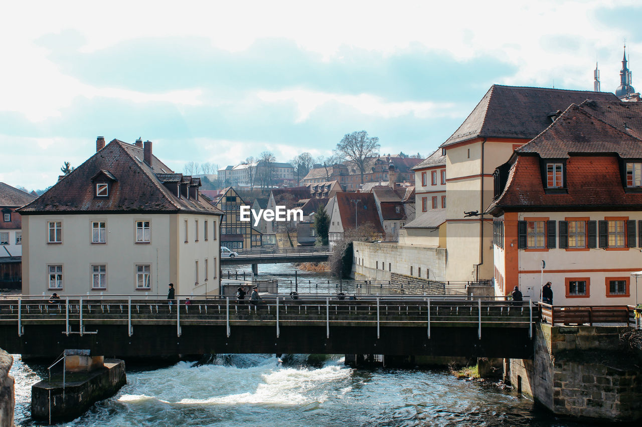 Houses by river in city against sky