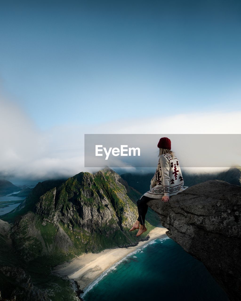 Girl sitting on rock looking at mountain against sky and beach