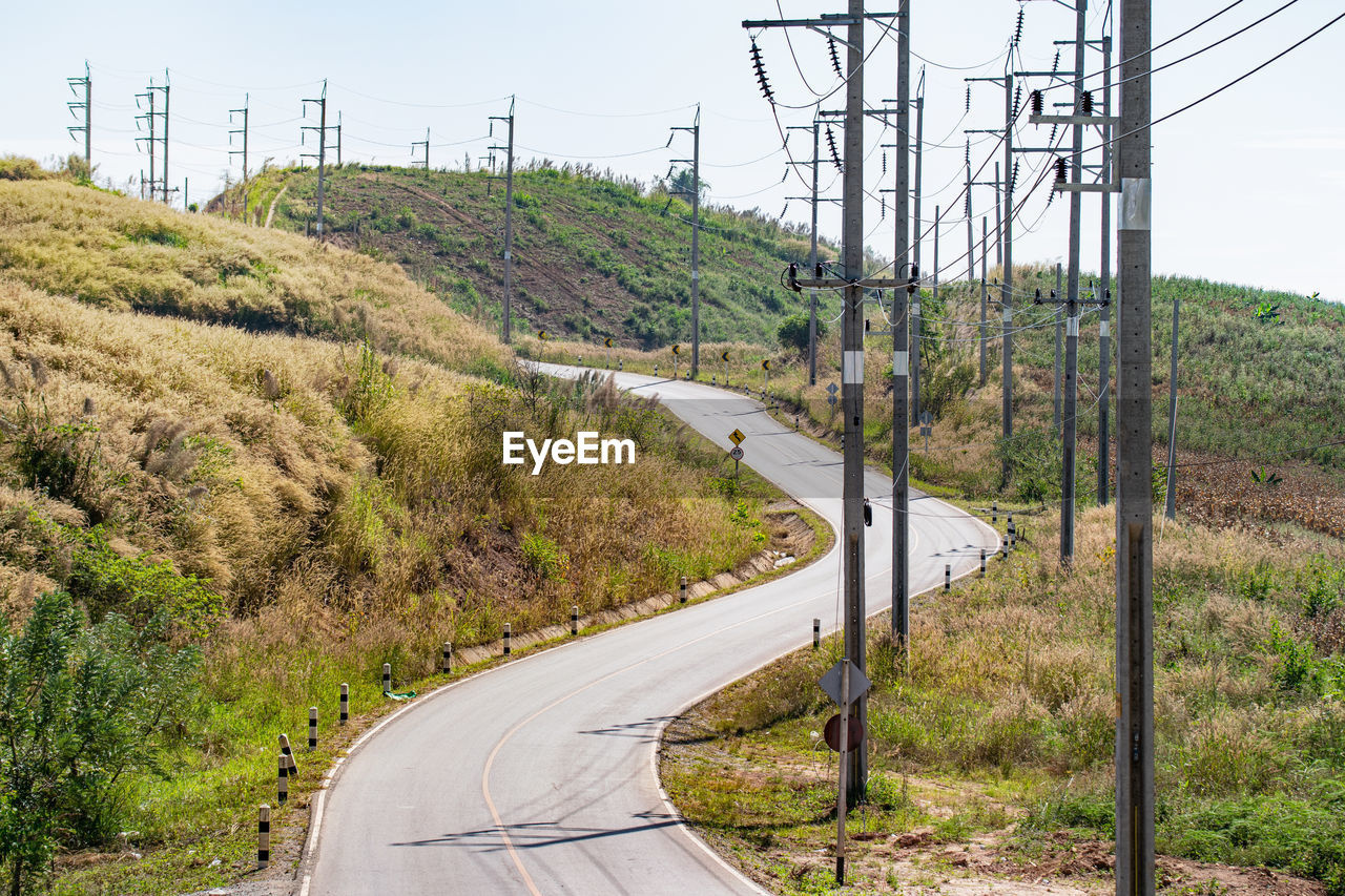 ROAD AMIDST TREES AND ELECTRICITY PYLONS AGAINST SKY