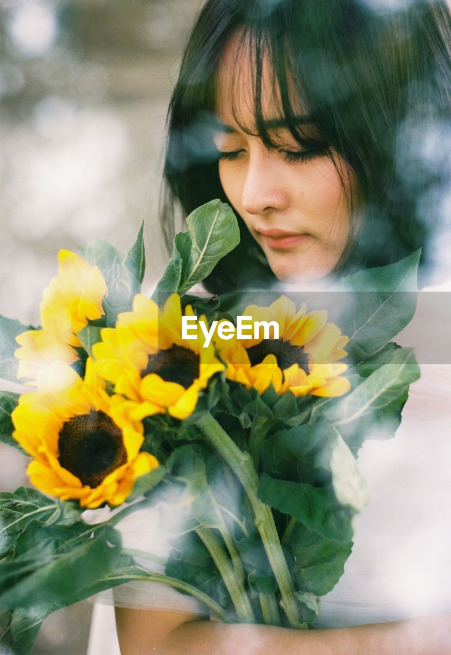 Woman holding sunflowers seen through glass window