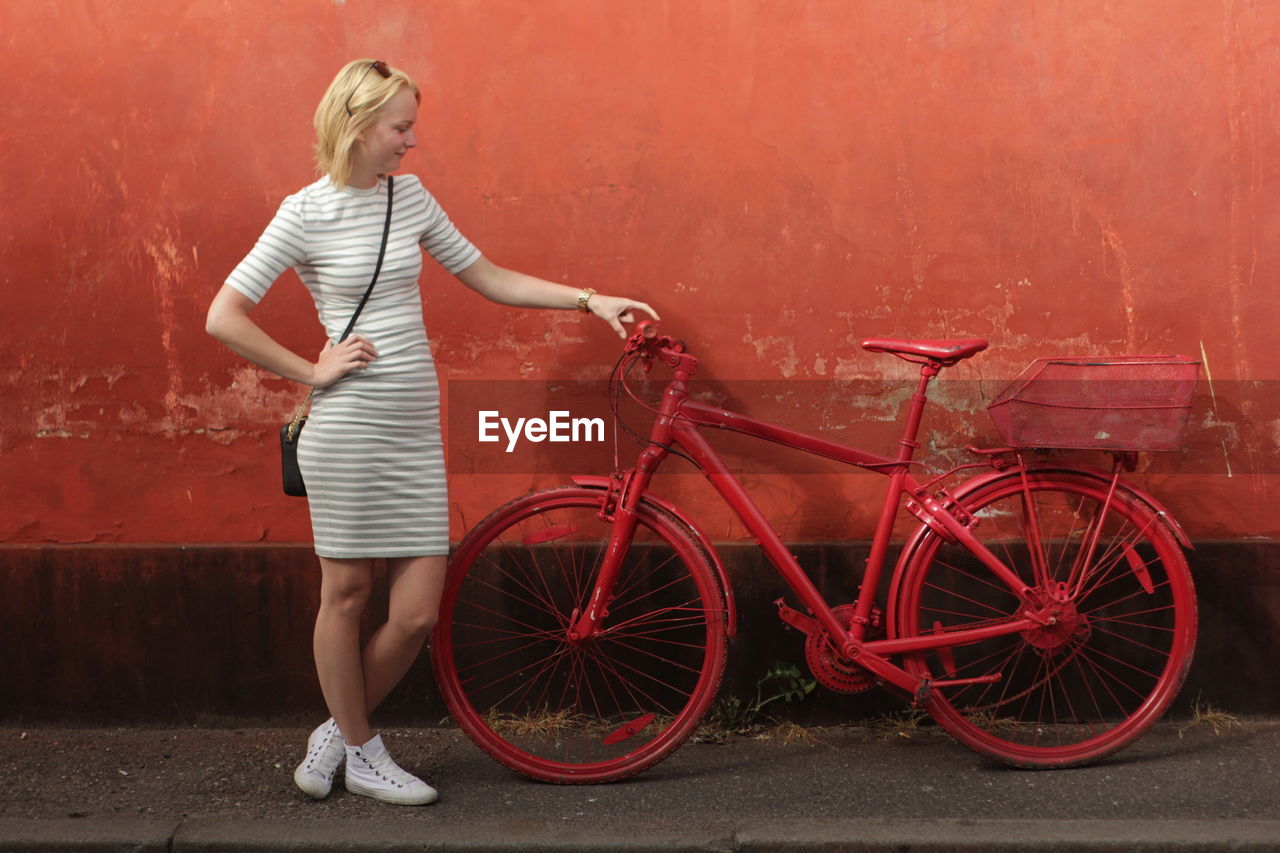 Full length of woman holding red bicycle while standing against wall