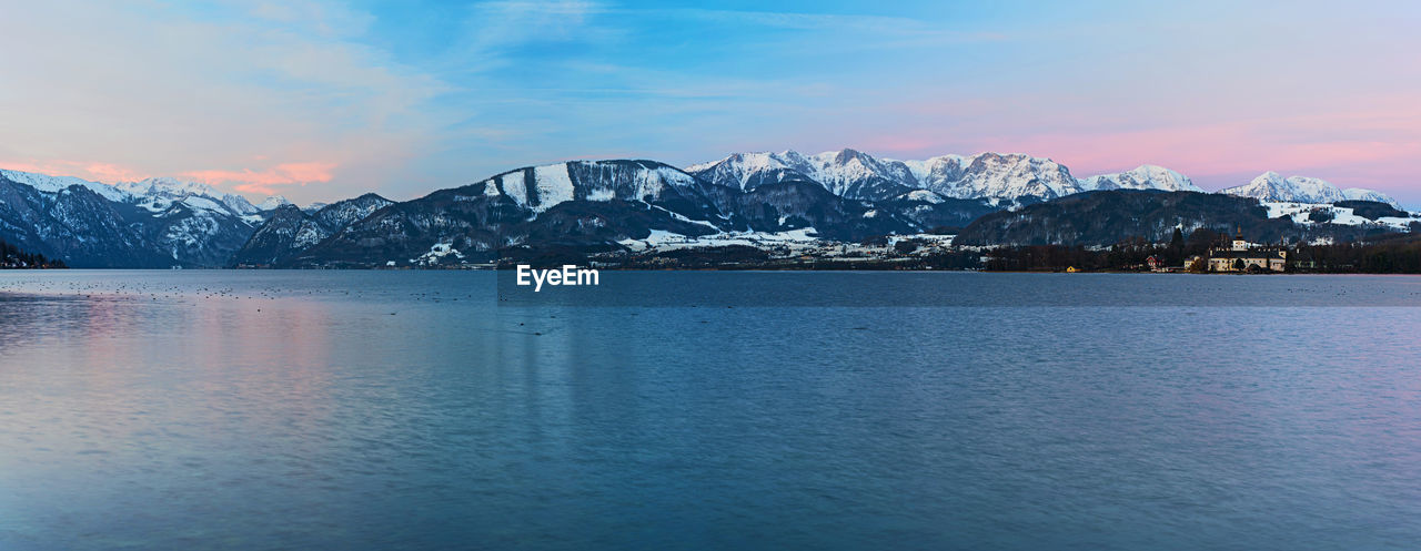 Scenic view of sea by snowcapped mountain against sky during winter