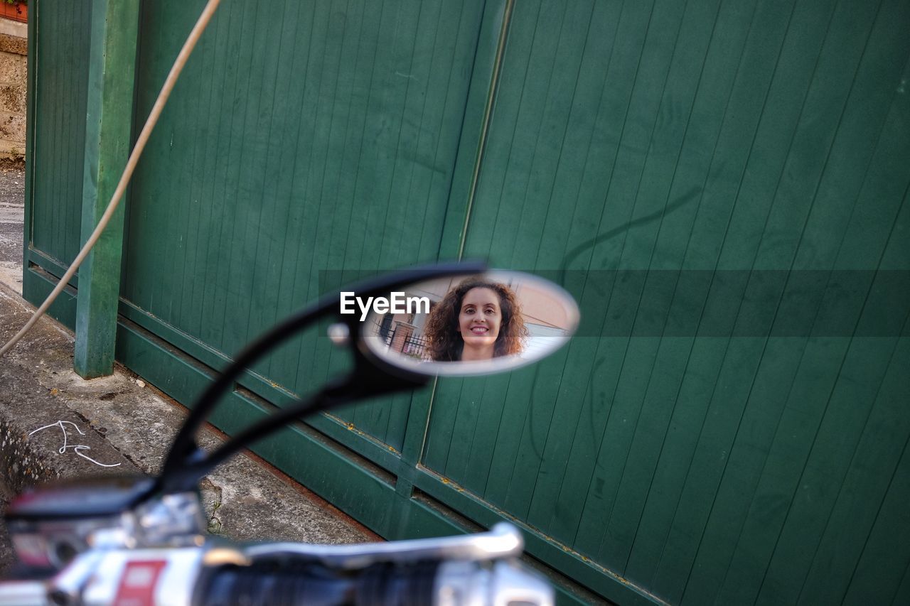 Smiling mid adult woman reflecting on side-view mirror