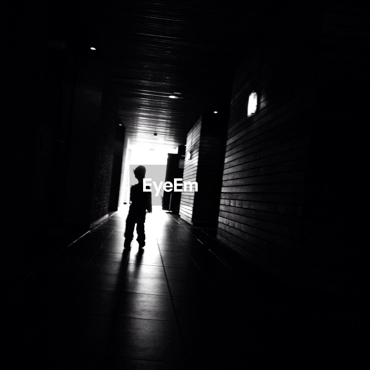 Silhouette boy standing in dark corridor