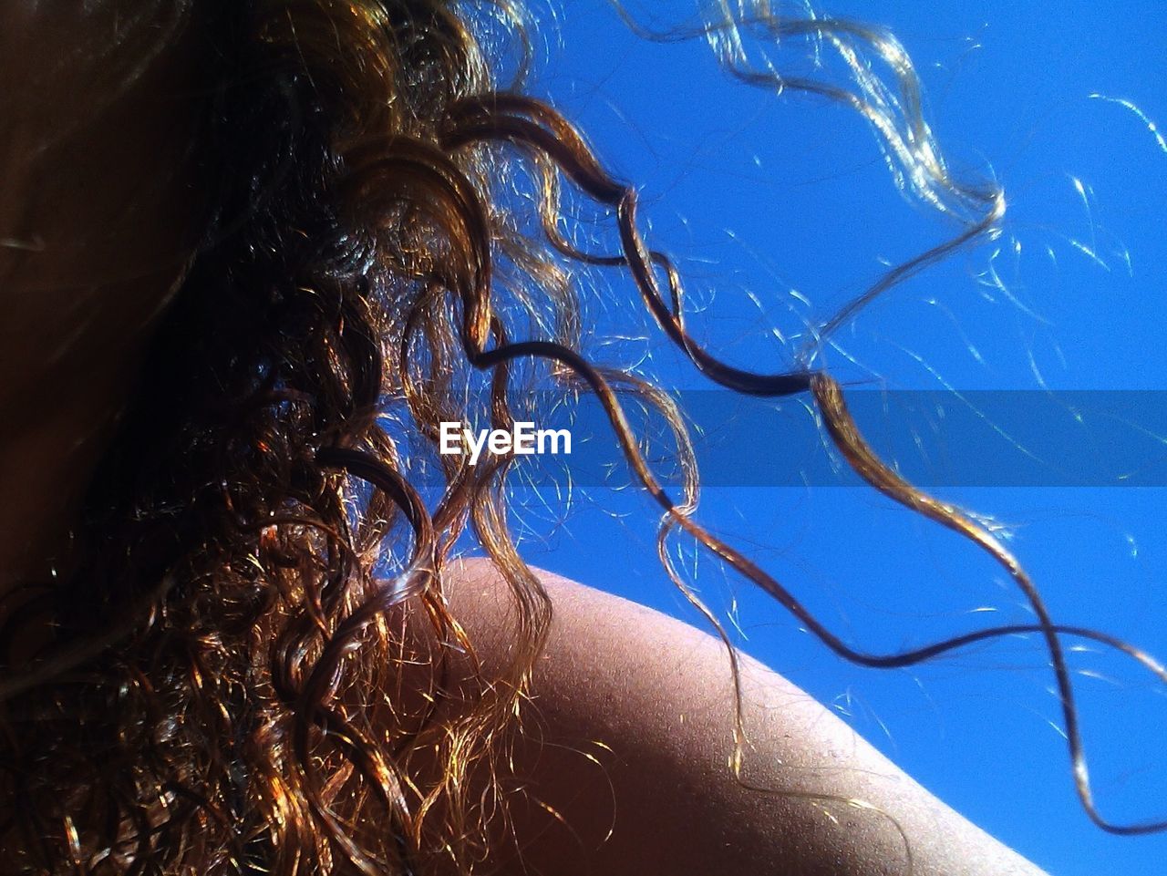 Cropped image of woman with curly hair against clear blue sky