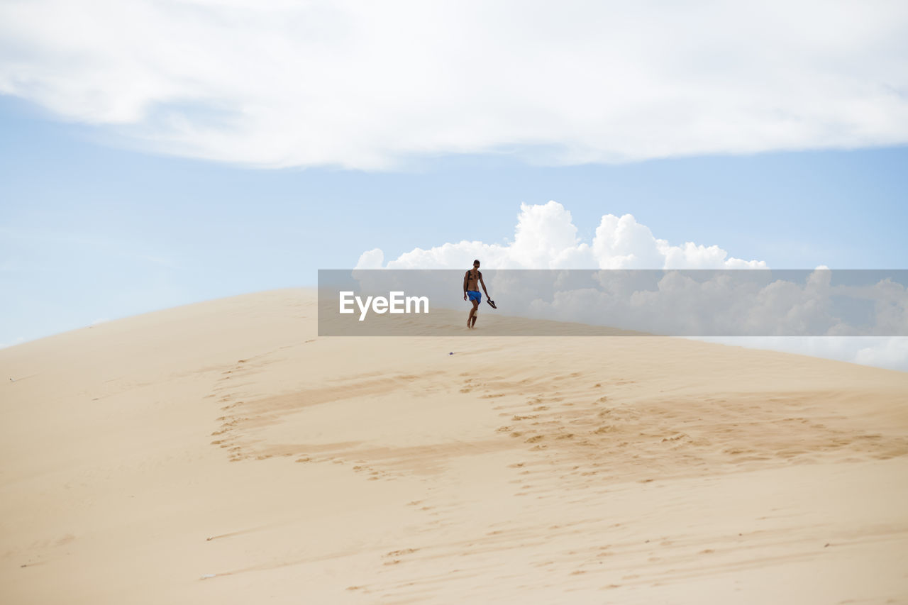 MAN ON SAND DUNE AGAINST SKY