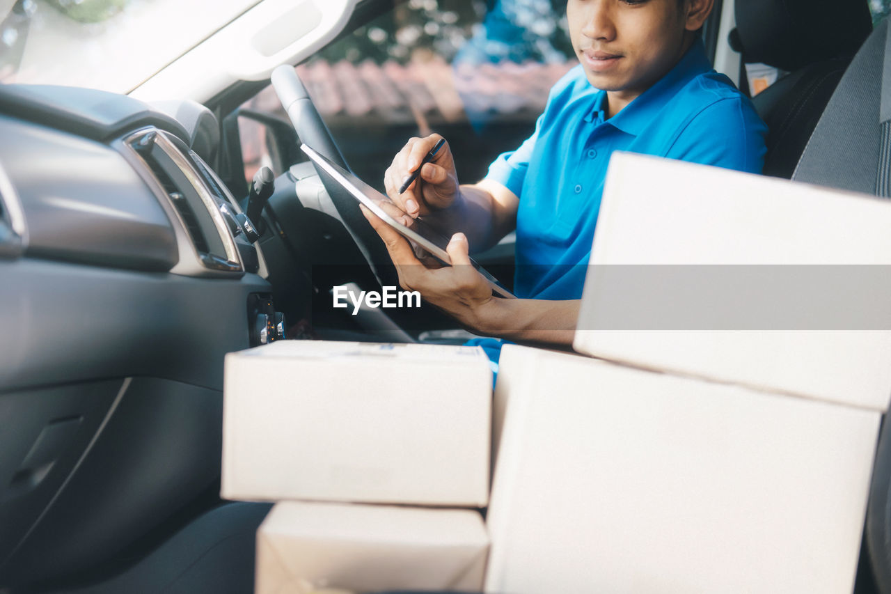 Delivery man using digital tablet while sitting in car