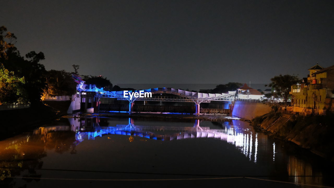 ILLUMINATED BRIDGE OVER RIVER AGAINST SKY IN CITY AT NIGHT