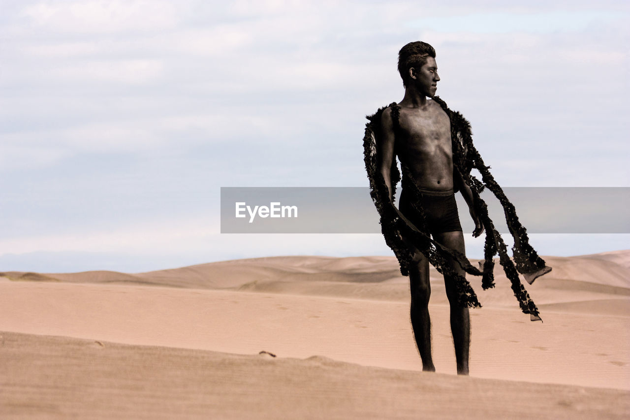 Teenage boy in costume on desert against sky