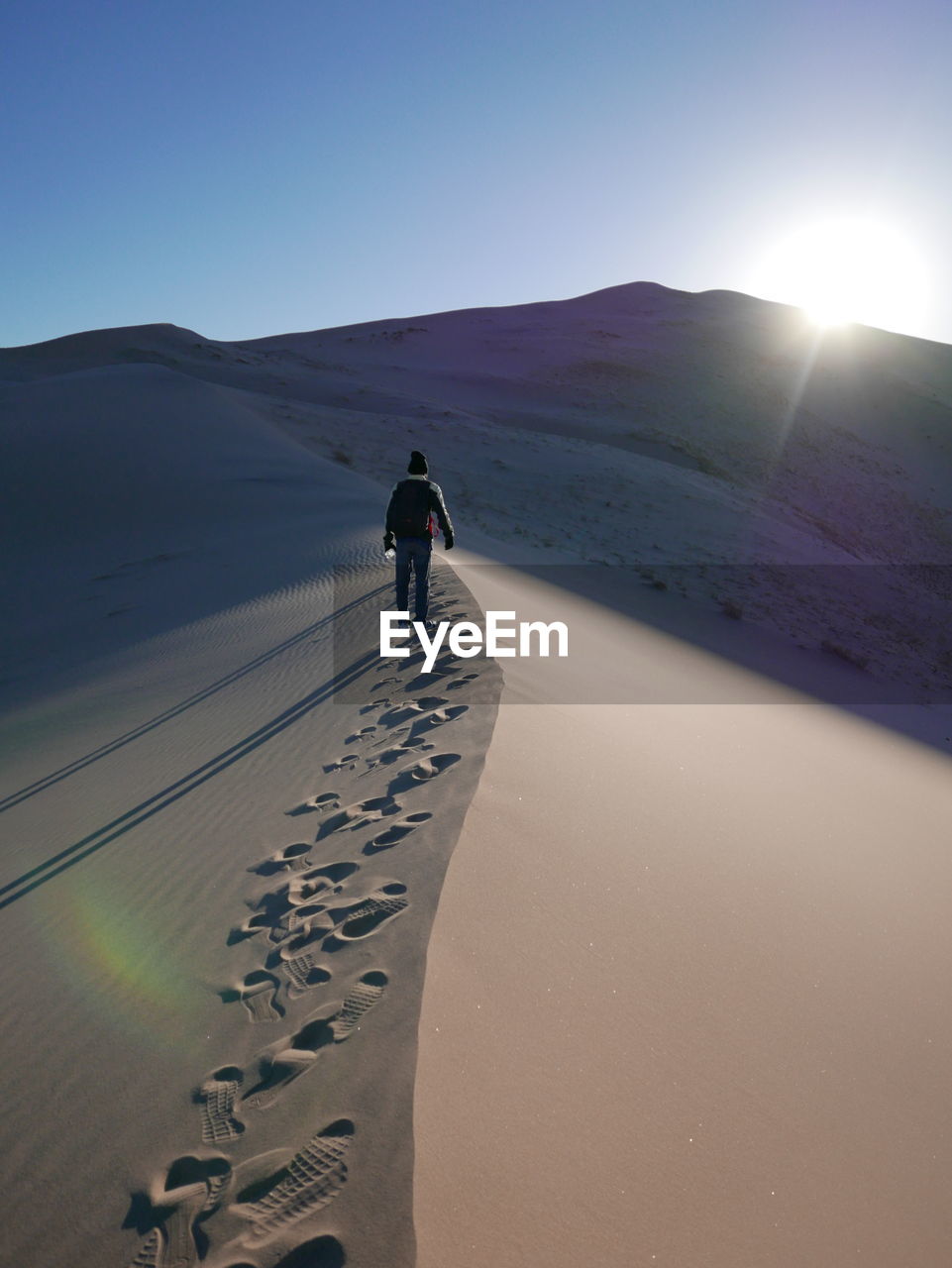 Rear view of man standing on sandy desert against sky