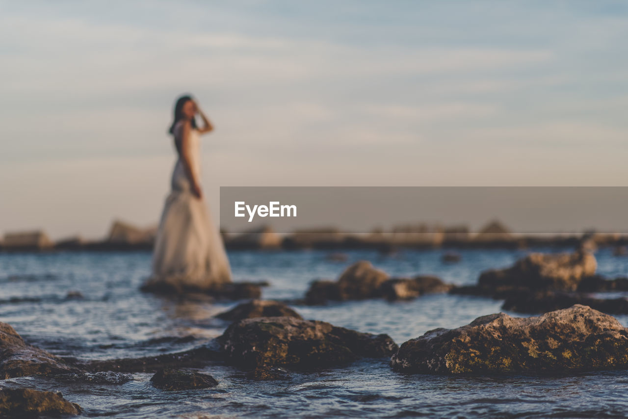 Woman on rock by sea against sky during sunset