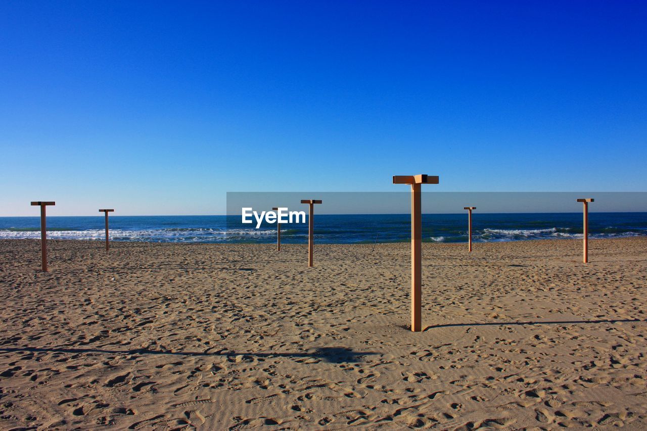 WOODEN POST ON BEACH AGAINST CLEAR BLUE SKY