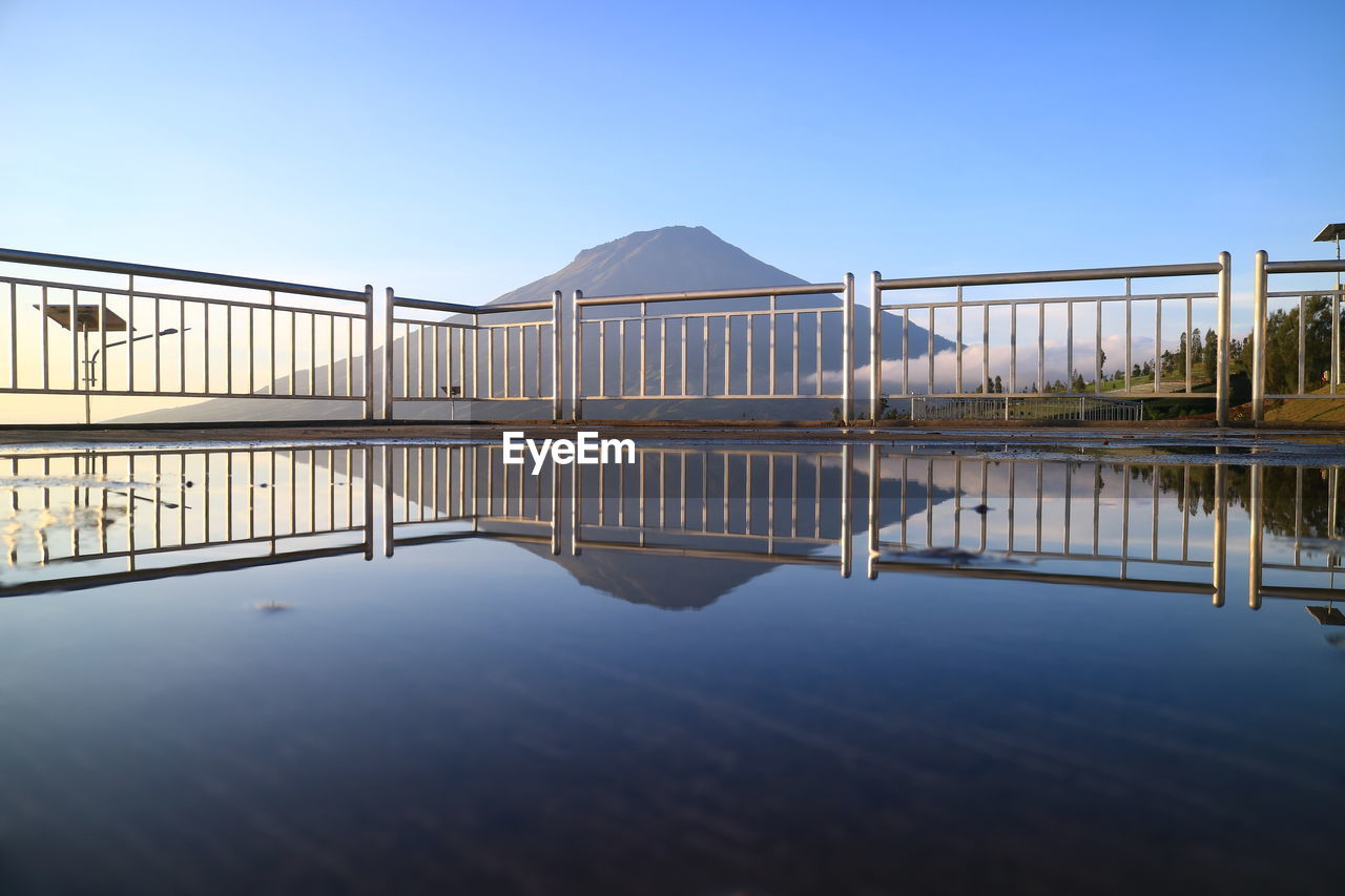 Reflection of bridge in lake against clear blue sky